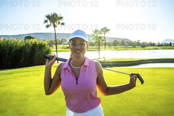 Female golfer smiling while holding a golf club, posing confidently on a lush green course near a tranquil water hazard and swaying palm trees