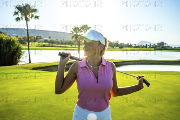 Female golfer confidently holding her golf club on her shoulders, posing gracefully on a stunning golf course during sunset