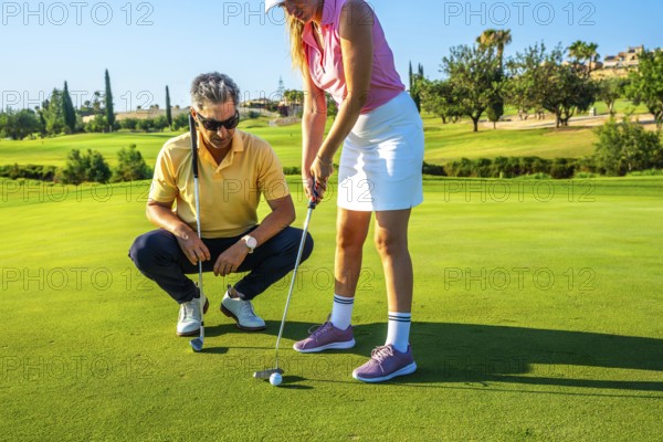 Golf instructor guides a woman on putting technique on a sunny golf course. They focus on improving her skills in a picturesque setting
