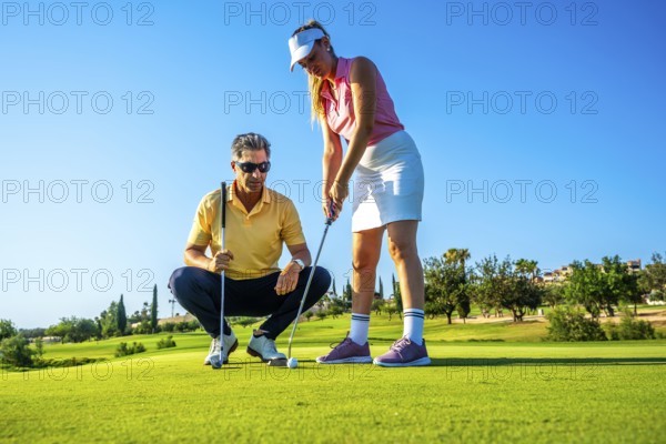 Golf instructor guides a woman on the putting green, focusing on technique under a clear blue sky. Perfect day for learning and practicing golf