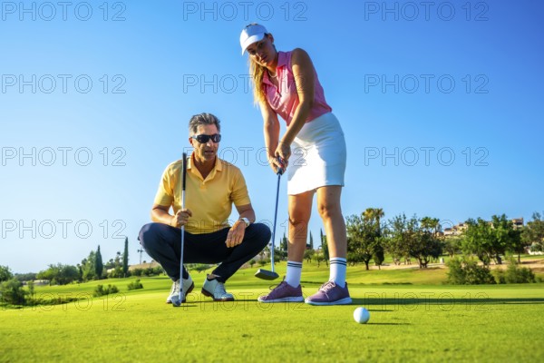 Female golfer receiving putting advice from her instructor under the warm sun, focusing on technique and skill improvement at the golf course