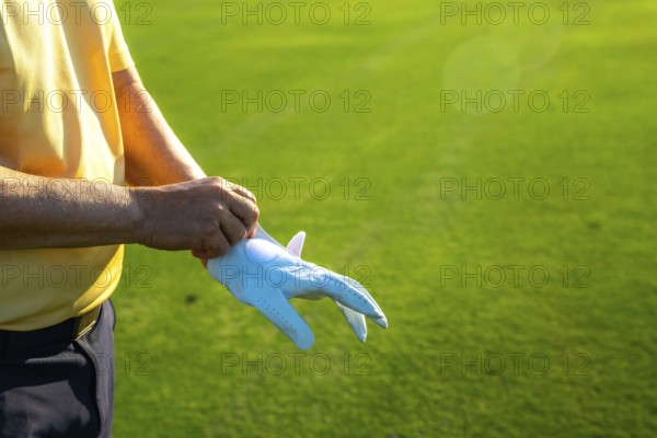Golfer putting on a white glove, getting ready for an exciting game on a lush, vibrant green golf course under the sunny sky