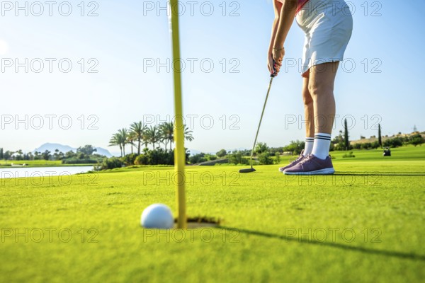 Female golf player putting ball on the green into the hole on a beautiful sunny day on a golf course