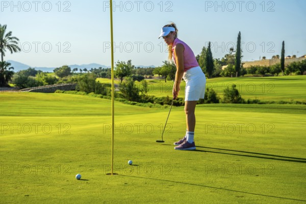 Professional golfer concentrating on putting the ball into the hole on a sunny day at the golf course
