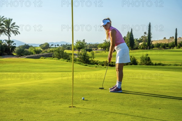 Professional golfer putting the ball on a lush green course under a bright sun, showcasing skill and focus in a competitive atmosphere