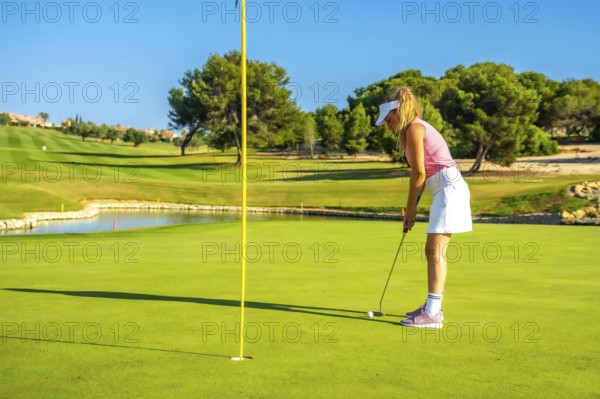 Female golfer concentrating on putting the ball into the hole on a sunny day at the golf course
