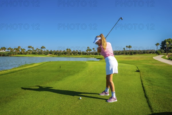 Woman golfer focusing intently on putting the ball on a sunny day, with a picturesque lake creating a serene backdrop