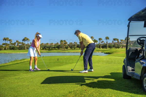 Father and daughter duo playing golf on a sunny day, surrounded by palm trees and a clear blue sky, enjoying quality time on the course