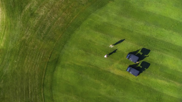 Aerial view of two golfers playing on a perfectly manicured green golf course, enjoying a sunny day of leisure and sport