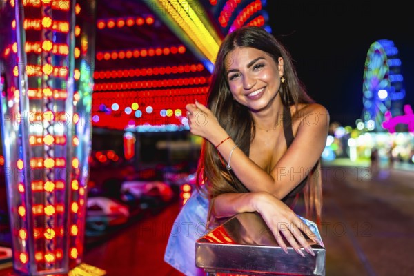 Happy young woman enjoying the vibrant atmosphere of a funfair, posing near colorful attractions at night