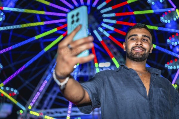 Tourist taking selfie with smartphone in front of illuminated ferris wheel at amusement park, enjoying nightlife entertainment