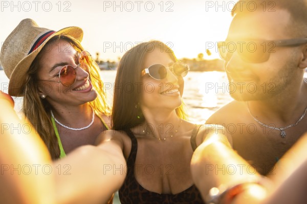 Cheerful young friends capturing a joyful selfie at the beach, reveling in the warmth of a summer sunset and creating lasting memories