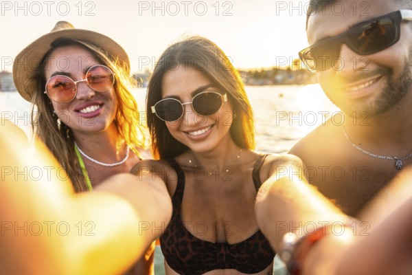 Cheerful young friends enjoying their summer vacation at the beach, capturing joyful moments together with a fun selfie during sunset