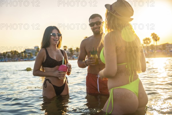 Three friends enjoying refreshing cocktails while having fun in the ocean at sunset, embracing the carefree spirit of summer and friendship