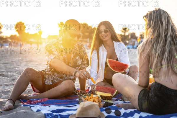Friends sharing laughter and enjoying juicy watermelon and sweet pineapple during a picturesque sunset picnic on the beach