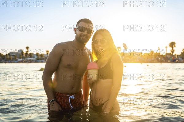 Young couple enjoying a refreshing drink in the sea at sunset, creating a romantic and carefree summer atmosphere