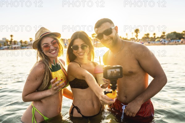 Three friends enjoying their summer vacation at the beach, taking a selfie with an action camera