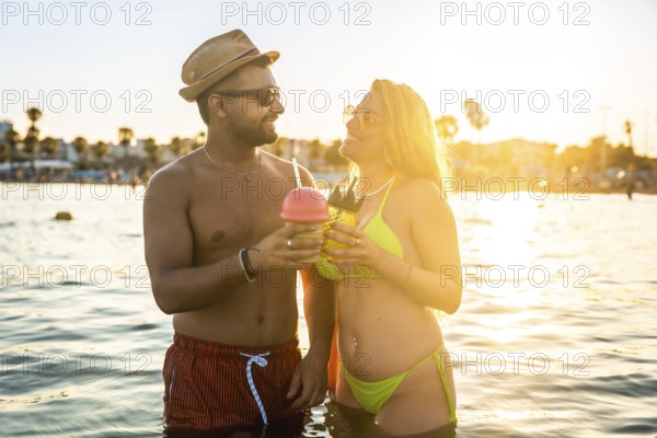 Tourists enjoying cocktails while wading in the ocean at sunset, embracing the warmth of summer and the joy of vacation bliss