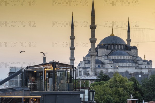Seagulls flying over a rooftop restaurant in istanbul, turkey, with the sultan ahmed mosque in the background at sunset