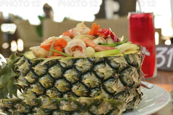 Pineapple fried rice with shrimp and vegetables served in a pineapple, a popular thai dish, alongside a refreshing drink in a restaurant