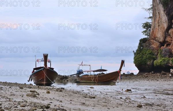 Two traditional thai longtail boats sit peacefully on the shore of railay beach, krabi, thailand, as the sun begins to rise, painting the sky with soft hues