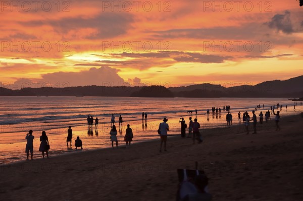 Tourists strolling along a picturesque beach in thailand at sunset, soaking in the vibrant orange sky and tranquil ocean waves