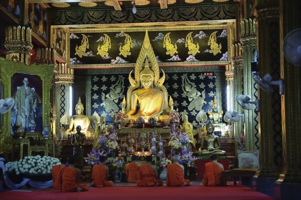 Group of buddhist monks praying in traditional orange robes inside ornate temple with golden buddha statue, showcasing thailand's rich spiritual heritage