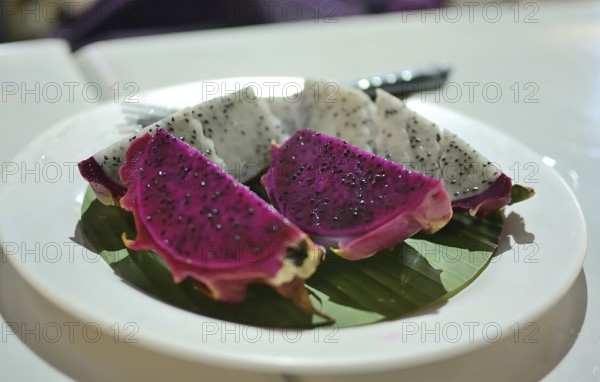 Vibrant slices of red and white dragon fruit are presented on a banana leaf atop a white plate, showcasing the exotic flavors of thailand