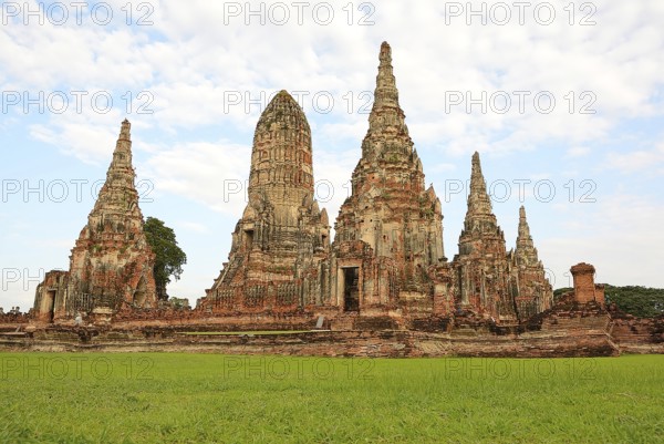 Scenic view of the historical wat chaiwatthanaram temple with its towering prangs and serene green lawn under a cloudy sky in ayutthaya, thailand
