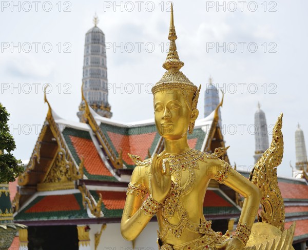 Golden kinnara statue praying with hands joined in a traditional thai greeting, inside the wat phra kaew temple complex in bangkok, thailand