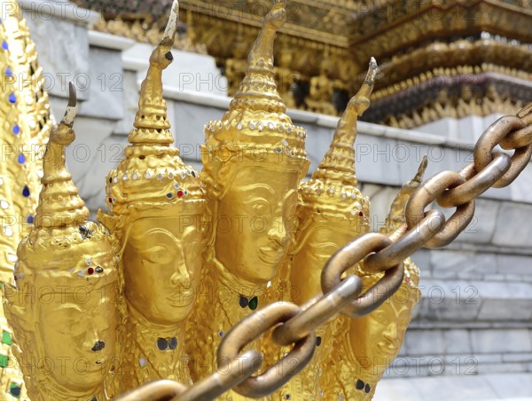 Golden garuda statues adorned with intricate metal chains stand prominently in the foreground, guarding a historic temple in thailand