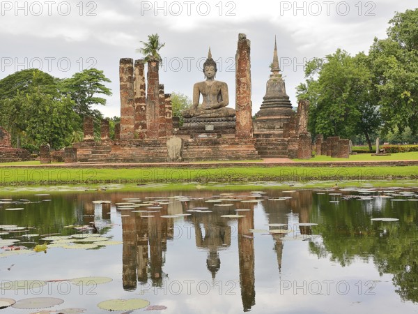 Serene buddha statue reflected in a pond at the sukhothai historical park, a unesco world heritage site in thailand