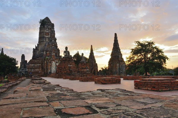 Serene buddha statues sit amidst crumbling temple ruins, bathed in the golden light of a beautiful sunset in thailand