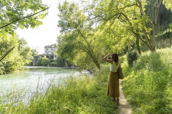 Woman enjoying a sunny day walking along the gave d'oloron river in sauveterre de bearn, a picturesque medieval village in the french pyrenees