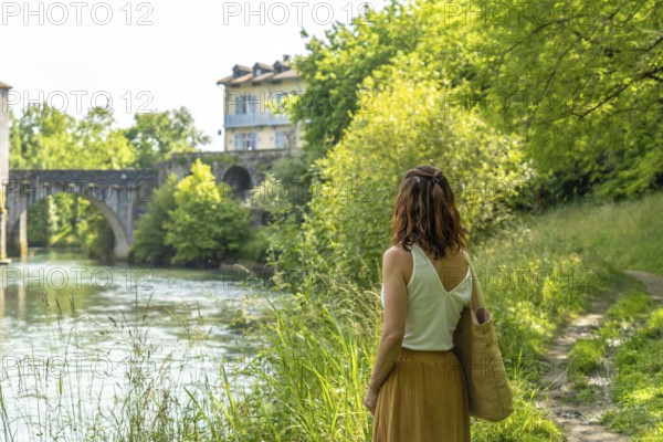 Woman enjoying the scenic view of the gave d'oloron river and the historic bridge during a summer vacation in sauveterre de bearn, a charming village in the pyrenees atlantiques region of france