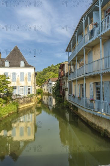 Picturesque canal reflecting traditional houses with blue balconies in salies de bearn, a charming village in the pyrenees atlantiques region of france