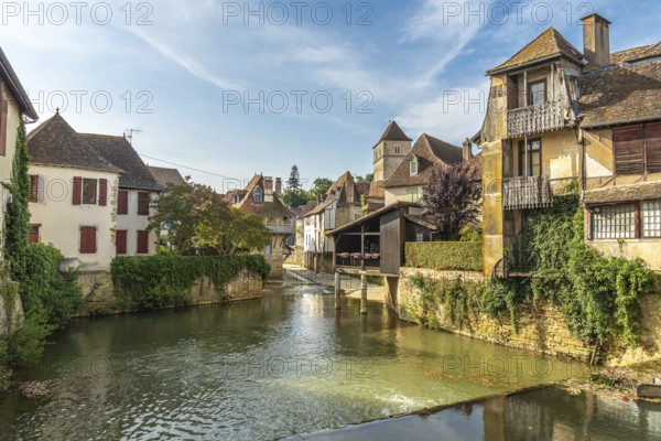Traditional houses lining the serene river in salies de bearn, france, create a charming reflection on a sunny day