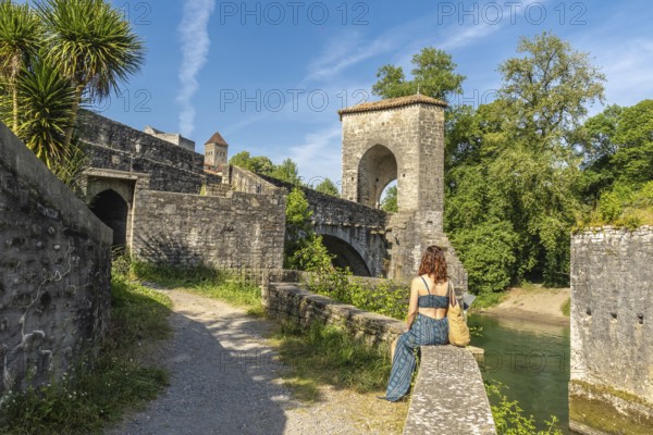 Young woman enjoying the scenic view of the historic bridge and fortifications in sauveterre de bearn, a charming medieval town in the pyrenees atlantiques region of france
