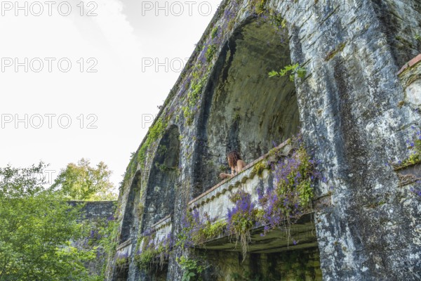 Tourist admiring the landscape from a balcony of an ancient aqueduct covered in vegetation in sauveterre de bearn, france