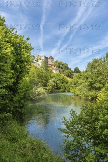 Lush vegetation surrounds the gave d'oloron river with sauveterre de bearn reflecting on the water surface on a sunny day