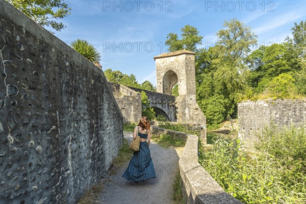 Tourist walking on a sunny day towards the medieval bridge of sauveterre de bearn in france, enjoying summer vacation