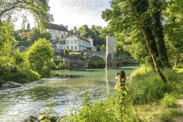 Tourist taking pictures of the gave d'oloron river and the old bridge in sauveterre de bearn, a picturesque medieval village in the french pyrenees