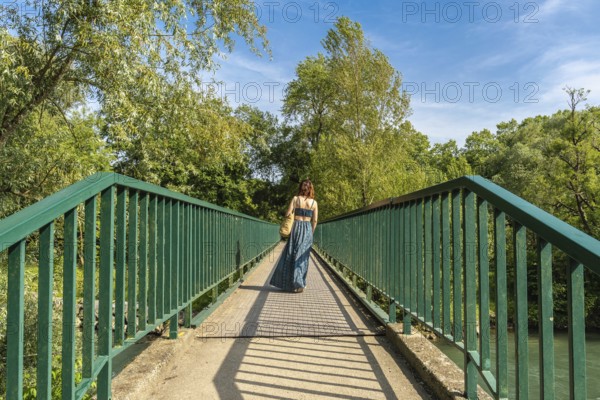 Woman walking away on a pedestrian bridge over gave d'oloron river, visiting sauveterre de bearn in france on a sunny summer day