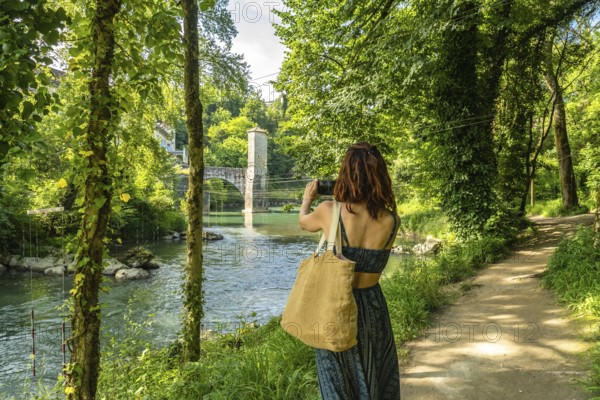 Tourist photographing the gave d'oloron river and its fortified bridge in sauveterre de bearn, a charming medieval village nestled in the heart of the french pyrenees