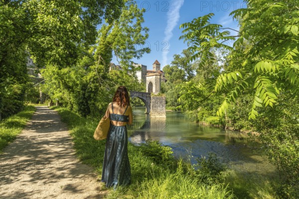 Tourist admiring the medieval bridge and the church of saint andre in sauveterre de bearn, a picturesque village in the pyrenees atlantiques region of france