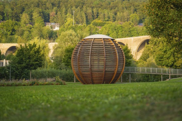 Large wooden ball in front of a bridge, surrounded by green trees and grassland, Nagold, district of Calw, Black Forest, Germany