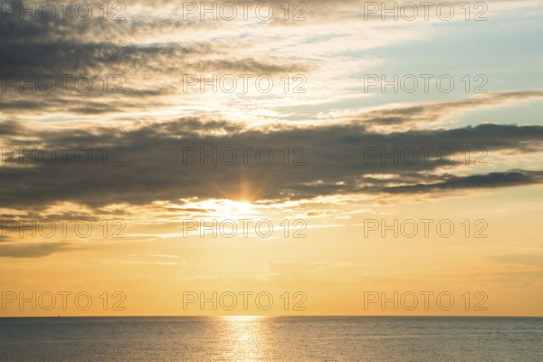 Picturesque sunset over the sea with soft clouds and golden light, sun star, clouds, reflecting light on the shining water and calm atmosphere, warm atmosphere, sea in soft colours, peaceful, orange and gold, wide horizon, cloud gap, dark, grey clouds, island dune, Helgoland, district Pinneberg, Schleswig-Holstein, North Sea, Germany