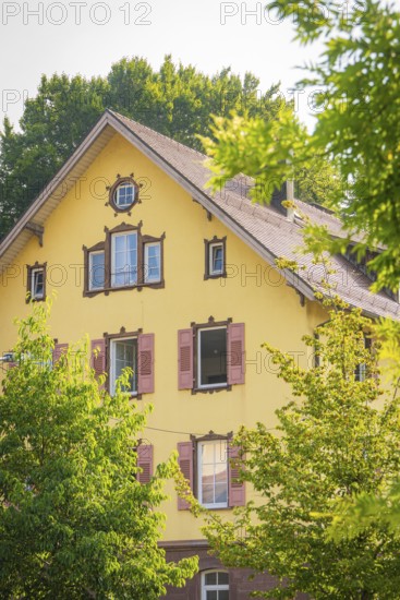 Yellow house with red shutters, surrounded by green trees under a summer sky, Nagold, district of Calw, Black Forest, Germany