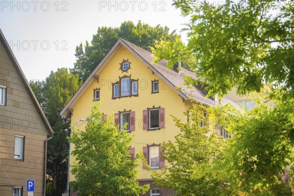 Yellow house with decorated shutters surrounded by green trees under a blue sky, Nagold, district of Calw, Black Forest, Germany