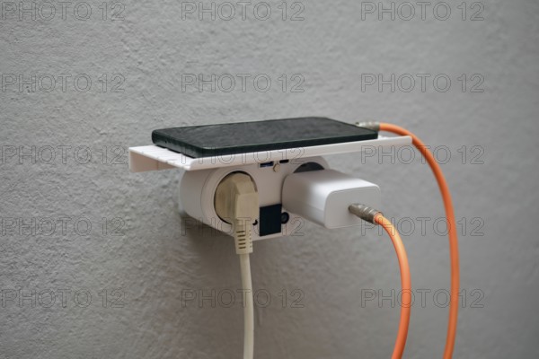 A smartphone rests on a wall-mounted charging station with an electrical outlet below